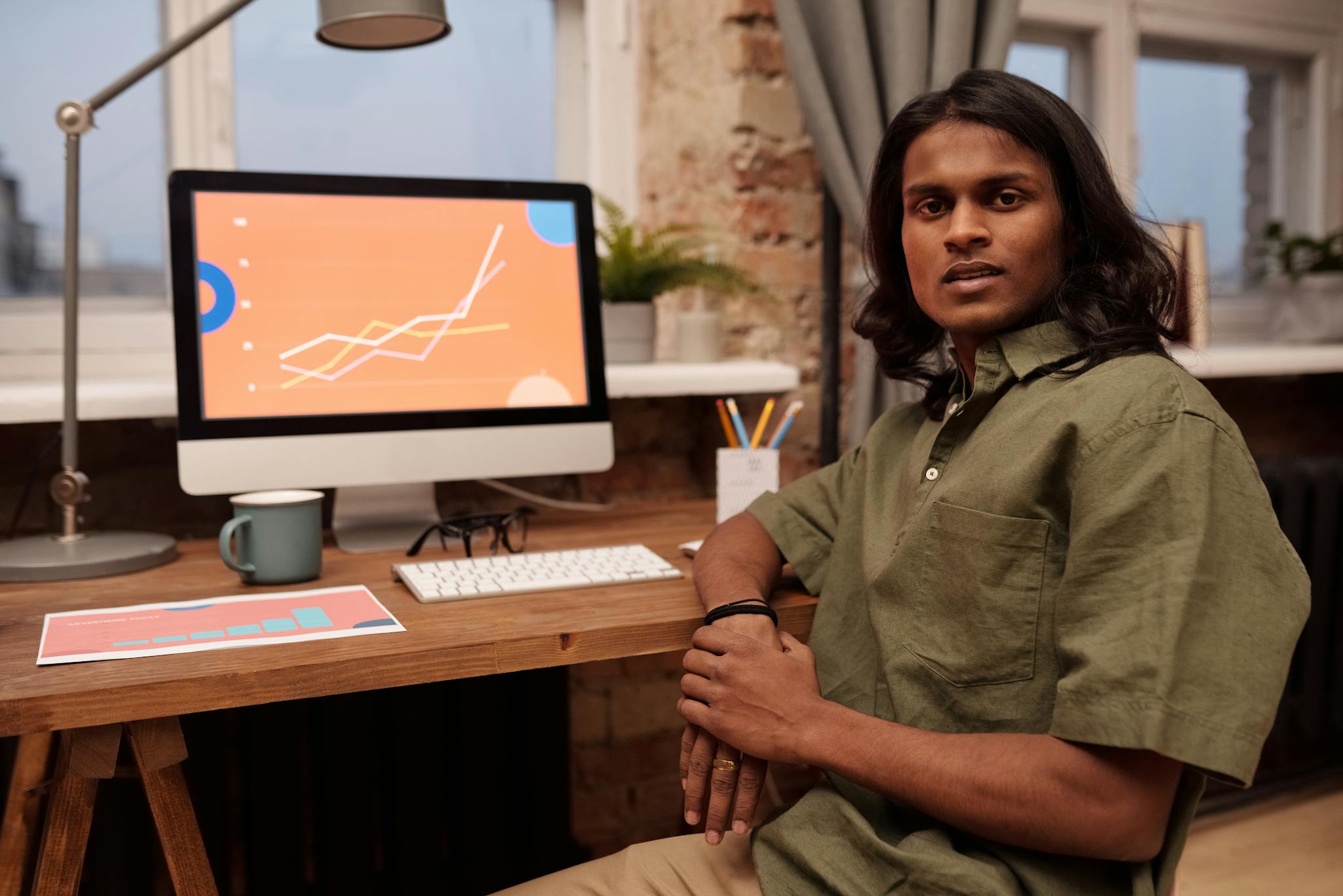 A young professional working in a home office setting, analyzing data charts on a computer screen.